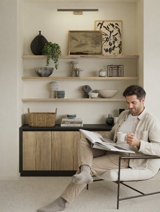 A man sat reading in a room with shelves and storage space
